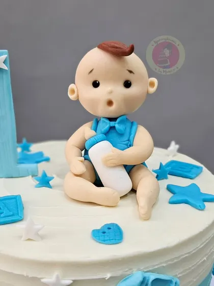 A close-up of the adorable baby boy figurine for a first birthday cake, complete with a milk bottle.
