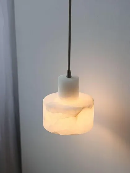 A simple, cylindrical pendant light made from solid marble. The soft glow through the stone creates a warm and calming ambiance.