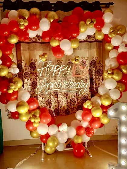 A classic anniversary decoration for a home celebration. A heart-shaped balloon arch in red, white, and gold is paired with a light-up number '1' for a first anniversary.