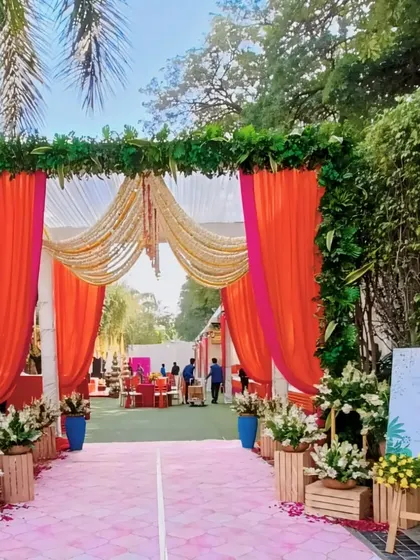 A beautiful entrance for a Mehendi Mela, with orange and pink drapes framed by lush greenery, setting a festive and welcoming tone.