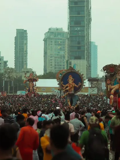 A wide view of Girgaon Chowpatty, filled with thousands of devotees and multiple large idols against the backdrop of Mumbai's skyscrapers.