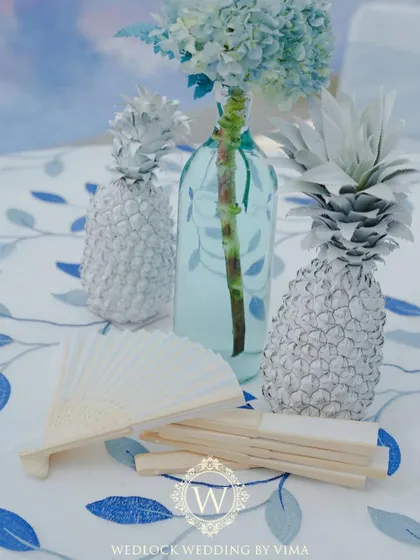 The details of our tropical pool party decor. The tables featured custom blue and white linens, with centerpieces of white-painted pineapples and blue-tinted water bottles holding fresh flowers.