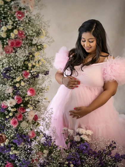 A quiet moment of connection. The mom-to-be looks down at her belly with so much love, her pink gown blending beautifully with the floral decor.