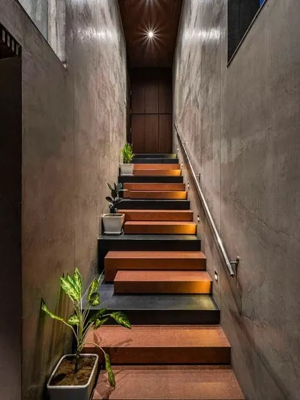 The interplay of raw materials can create powerful designs. We are inspired by staircases that use a simple palette, like the combination of concrete walls, terracotta-colored steps, and subtle step lighting seen here, to create a path that is both moody and beautiful.