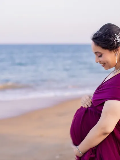 A serene and beautiful solo portrait of the mom-to-be, gazing peacefully at her baby bump against the vast ocean.