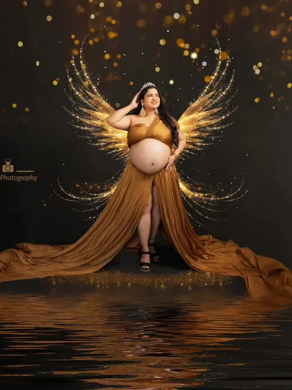 Embracing the glow of motherhood with elegance and grace. This golden goddess radiates pure magic with angel wings as she awaits her little miracle.