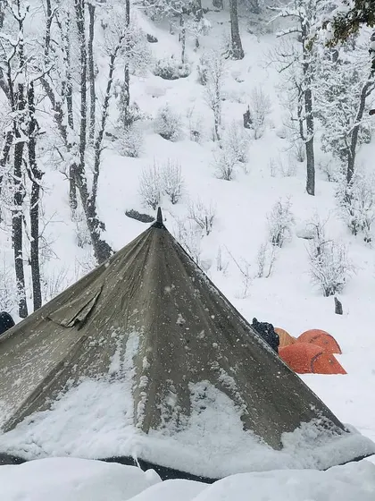 A close-up of the snow-dusted canvas tent, showing its resilience in the winter forest. This type of shelter offers a different, more traditional camping feel.