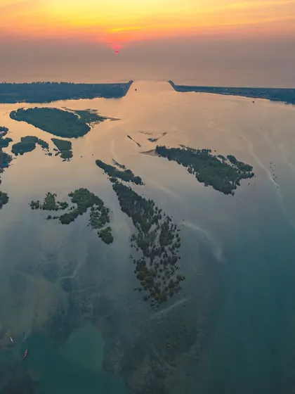 The sun sets over the vast backwaters of coastal Karnataka. The drone captures the intricate network of small islands and mangrove forests.