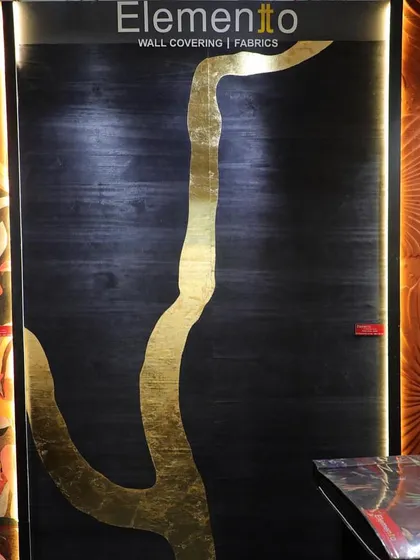 A dramatic wallcovering featuring a bold, abstract tree branch rendered in gold leaf on a dark, textured background. This design combines natural inspiration with luxurious materials for a striking effect.