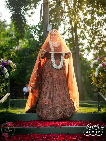 The bride's grand entrance, holding her Varmala and walking down an aisle covered in red rose petals.
