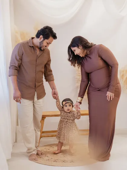 A precious moment of a baby's first steps. The proud parents hold their daughter's hands, guiding her as she walks on a small rug in the studio during her first birthday family session.