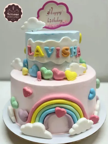 A lovely two-tier rainbow-themed cake. The pastel colors, fluffy clouds, and colorful hearts make this a cheerful and dreamy cake for a child's birthday.