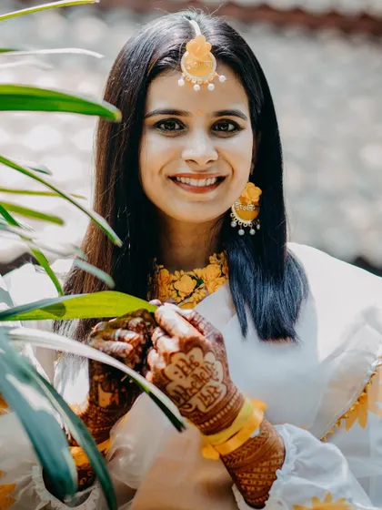 A smiling portrait of the bride during her Haldi ceremony. Framed by green leaves, this shot feels fresh, natural, and full of happiness.