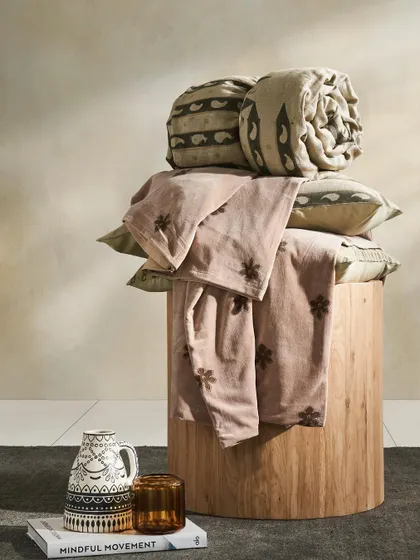 A still life composition of rolled quilts and patterned textiles on a wooden stool. This artistic arrangement is perfect for showcasing a new collection in a catalog or lookbook.