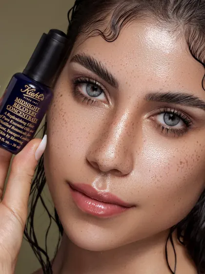 Here, the focus is on real, beautiful skin, complete with natural freckles. The model holds the Kiehl's Midnight Recovery Concentrate, creating a direct link between the product and the resulting dewy complexion. The wet-look hair adds to the overall feeling of hydration and freshness.