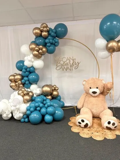 A minimalist and modern teddy bear setup with a golden ring backdrop. The teal, white, and gold balloon garland and jute rug create a chic and stylish look.