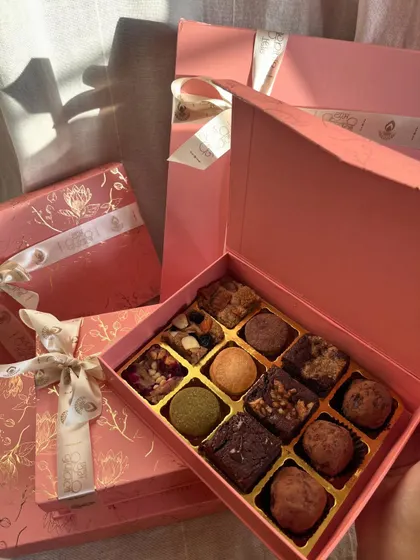 This is my Truffle Edition box, which includes my handmade dark chocolate truffles alongside the brownies and blondies. The sunlight here really shows off the beautiful pink and gold foil packaging.