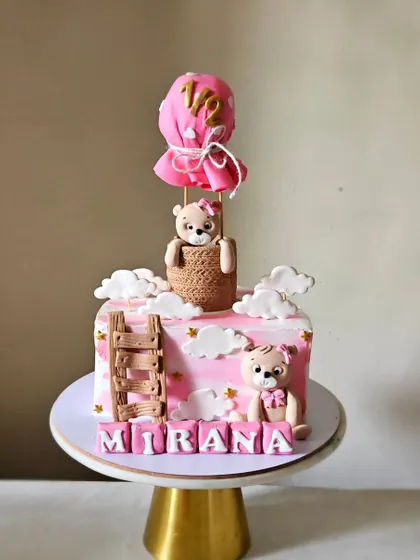 Celebrating a half birthday with this adorable hot air balloon themed cake. This square cake in shades of pink features two cute teddy bears, edible clouds, and a hot air balloon topper marking "1/2".
