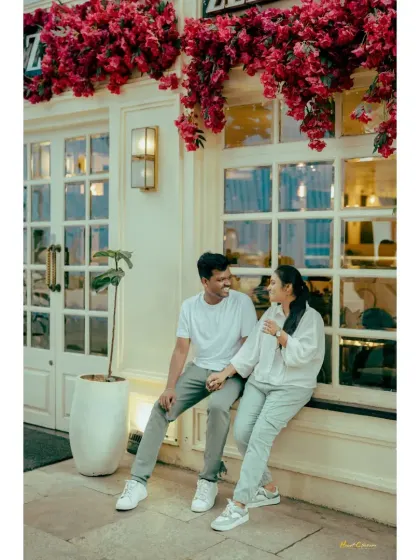 A couple holds hands while sitting on a cafe windowsill, sharing a happy, candid moment.