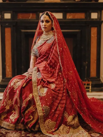 A bride seated in a regal pose, wearing a traditional red bandhani saree. This look is all about heritage and timeless elegance.