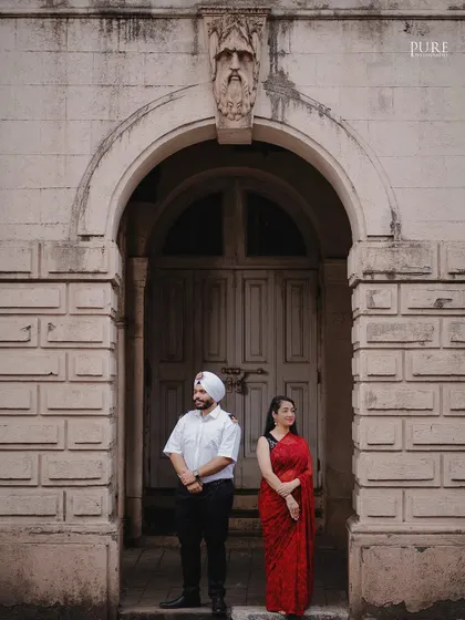 A formal portrait of Kanwaldeep and Avneet standing under a grand archway in Mumbai. The architectural details and their poised stance give this pre-wedding photo a touch of classic elegance.