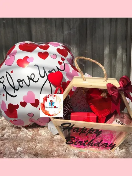 A romantic birthday hamper featuring a large "I love you" balloon and a hexagonal wooden box filled with red-themed gifts.