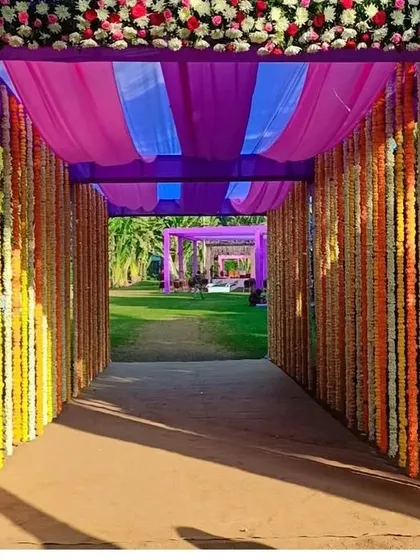 A view from inside the wedding entrance tunnel, looking out onto the lawn. The colorful flower strings and draped ceiling create a beautiful frame for the venue ahead.