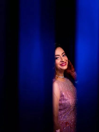 A happy and vibrant portrait of a woman in a sparkling pink dress. The creative use of blue pillar-like framing adds a unique and modern touch to the composition.