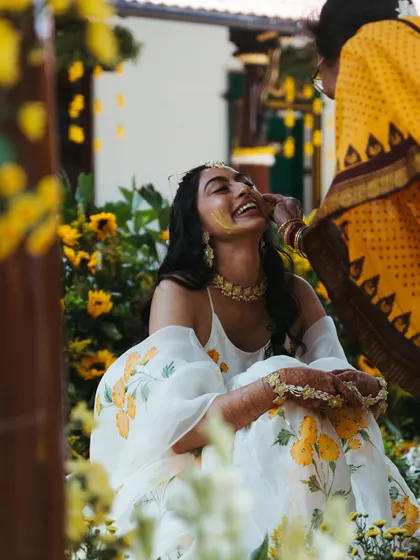 A candid moment of pure laughter as the bride gets turmeric paste applied to her face. Surrounded by sunflowers, her joy is infectious and beautifully captured.
