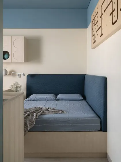 This son's room playfully fuses whimsy with modern minimalism. A cozy, upholstered bed nook in a deep blue invites rest, set against a backdrop of soft blue and cream walls.