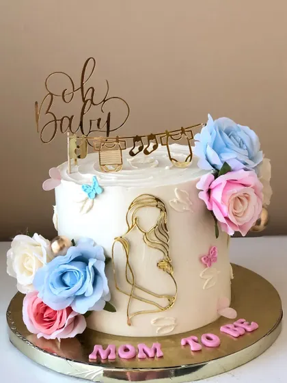 A beautiful "Mom to Be" cake with a modern gold-line illustration, surrounded by blue and pink flowers.