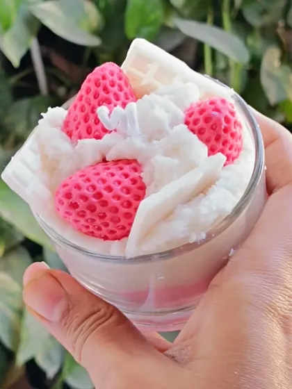A close-up, hand-held view of the strawberry ice cream candle against a leafy background.