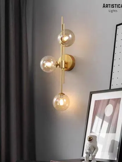 This vertical three-globe sconce adds a touch of modern glamour next to a bedside or in a hallway. The combination of clear glass globes and a linear brass structure creates a dynamic and stylish lighting fixture.