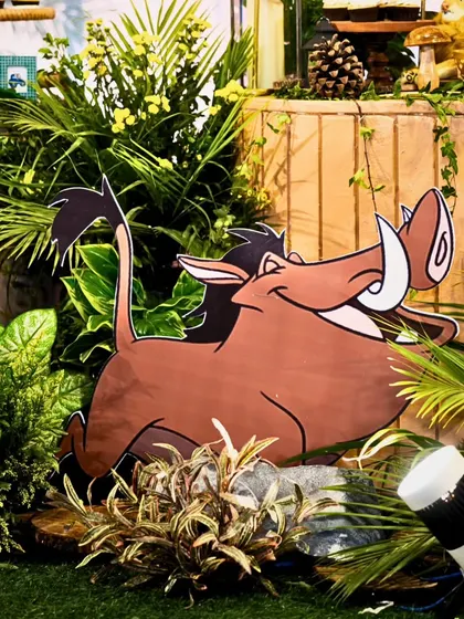 A Pumbaa cutout is nestled amongst lush greenery and spotlights, bringing a fun and recognizable character from The Lion King to the party's decor.