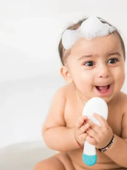An adorable shot of a baby in a tub, holding a brush with a happy expression. The clean, white setting emphasizes purity and safety, which is essential for baby product photography.
