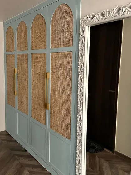 A custom-designed wardrobe with arched panels and cane webbing, finished in a soft powder blue. The long brass handles add a touch of modern elegance to this vintage-inspired piece.