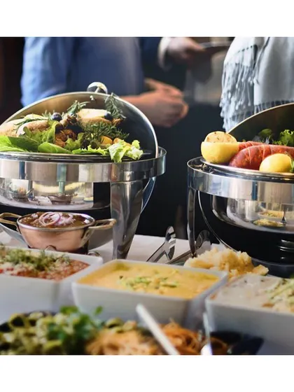 A classic buffet line with stainless steel chafing dishes. This setup is ideal for corporate lunches and seminars, ensuring food is kept warm and served efficiently and professionally.