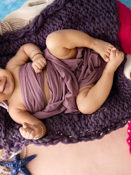 A happy, smiling baby enjoying her mermaid-themed photoshoot. This overhead shot captures her joyful expression and the beautiful textures of the setup.