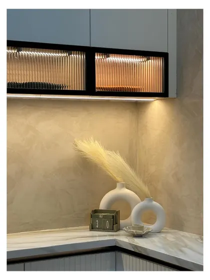 A beautifully styled corner where aesthetics are everything. The fluted glass cabinets with internal lighting, the soft texture of the wall, and the minimalist white vases create a moment of quiet, curated beauty.