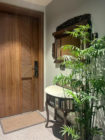 This entryway features a blend of traditional and biophilic design. An intricately carved mirror and console table are paired with a tall bamboo plant, bringing a touch of nature indoors.