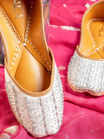 A clean and elegant shot of a white, sequined jutti. We use soft lighting and simple backgrounds to let the product's design and texture take center stage.