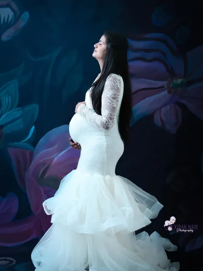 A profile shot of a mom-to-be in a white lace gown against a dark floral backdrop, creating a beautiful contrast.