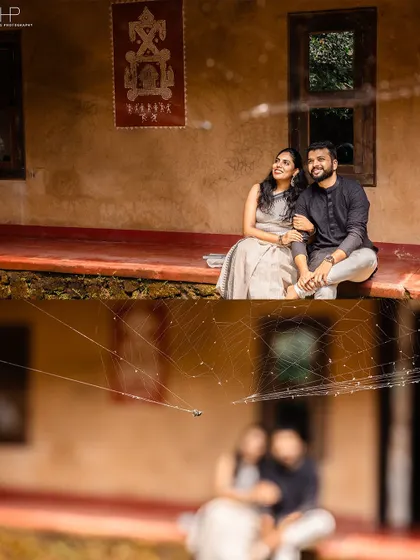 A unique composition where the couple is seen through a spiderweb in the foreground. This artistic choice adds an interesting layer to a romantic portrait on the veranda of a traditional home.