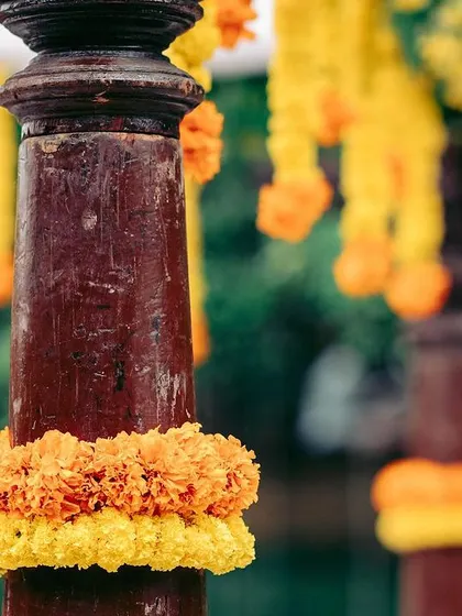 A close-up of a traditional wooden pillar wrapped in marigold garlands, highlighting the rich textures and colors of the decor.