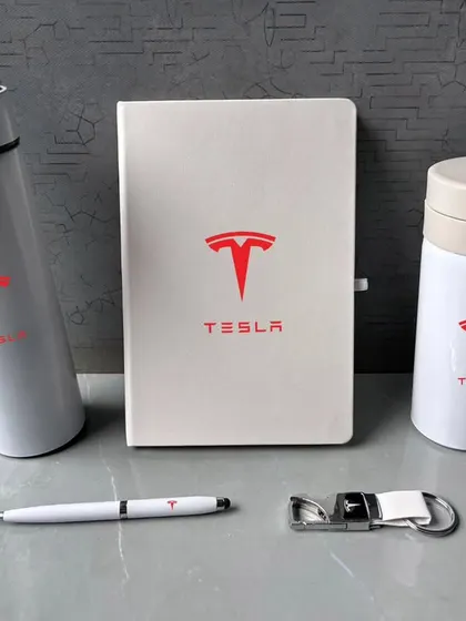 Here are the items from the white Tesla gift set, displayed to show the quality of each piece. The set includes a temperature flask, a travel mug with a spill-proof lid, a diary, a pen, and a keychain.