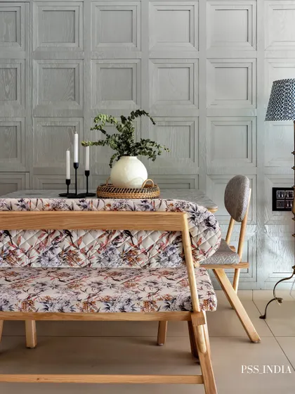 Texture and pattern play define this unique dining space. A floral upholstered bench is paired with a paneled grey wall and a rustic floor lamp, creating an eclectic yet cohesive look.