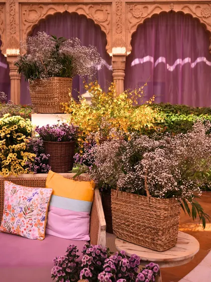 A cozy seating nook at the Jaisalmer Mehendi, with wicker furniture, colorful striped cushions, and baskets overflowing with flowers.