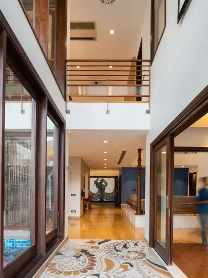 The entrance corridor of the Ashraya Residence is a dramatic double-height space. It sets the tone for the home's spatial experience, with a strong visual axis drawing the eye towards a mural at the far end.