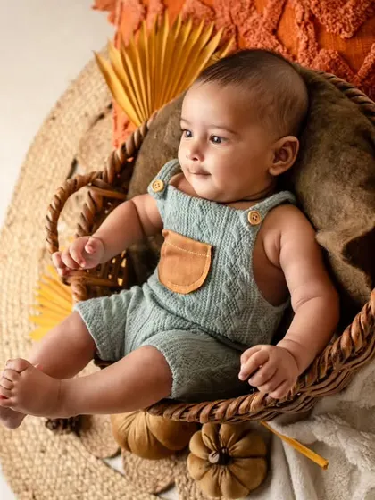 A calm and curious 4-month-old baby relaxing in a basket. The autumn-themed props add a warm and cozy feel to this infant portrait.