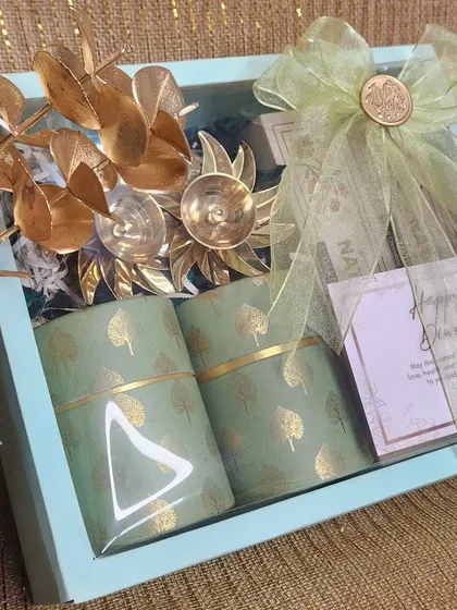 An elegant Diwali gift box in a soothing pastel blue. It contains two beautifully packaged jars and silver floral accents, tied with a delicate green ribbon.
